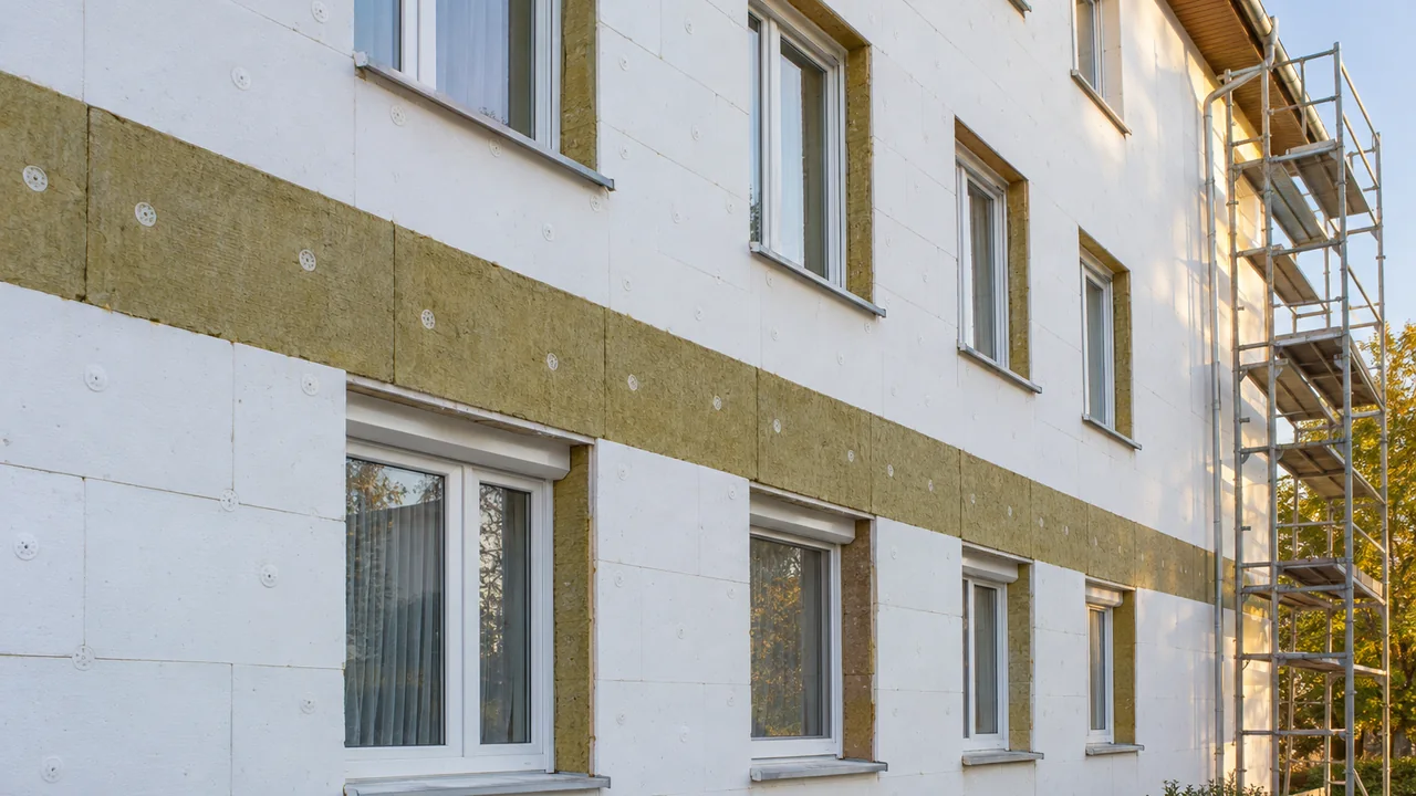 Illustration: a three-storey apartment facade under renovation; white EPS boards with plate anchors, a horizontal stone wool band above the windows, stone wool in the window reveals, and scaffolding on the right